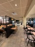Modernes Restaurant mit Holztischen, schwarzen Stühlen und einem Buffetbereich.