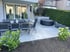 Moderne Terrasse mit grauen Fliesen, Esstisch-Garnitur, rundem Whirlpool und grüner Hecke im Hintergrund.