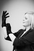 Eine blonde Frau im Profil zieht sich schwarze Einweghandschuhe an.