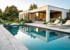 Moderner weißer Bungalow mit großen Fenstern, Garten, Liegestühlen und klarem rechteckigem Swimmingpool am Abend.