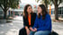 A teacher and a student sitting on a bench in a school courtyard having a conversation.