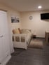 Schlafzimmer mit weißem Bett, Schrank, Teppich, Wanduhr, Fernseher und Bild.