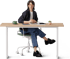 Eine sitzende Frau mit dunklem Blazer und blauer Hose an einem Schreibtisch mit Laptop und Notizbuch.