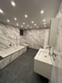 Modernes Badezimmer mit Marmorfliesen, dunklem Boden, Badewanne, WC, Waschbecken und Spiegel Reutte