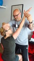 Ein Physiotherapeut führt bei einer Patientin einen kinesiologischen Muskeltest am erhobenen Arm durch.