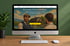 Ein iMac auf einem Schreibtisch zeigt eine Immobilien-Website mit zwei Männern vor einem Haus und Text zur Immobilienvermietung.