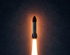 Eine Rakete startet in den Nachthimmel, ein heller Feuerschweif leuchtet vor einem sternenübersäten Hintergrund.