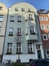 Helles, fünfstöckiges Wohnhaus mit Erker und Blumenkästen an den Fenstern.