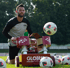 Ein Fußballspieler kniet neben einer Fußball-Schussmaschine von Globus, die einen Fußball in die Luft schießt.