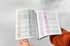 Zwei Hände halten ein offenes Buch mit Diagrammen und Statistiken vor einem weißen Hintergrund.