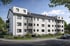 Modernes weißes Mehrfamilienhaus mit grauen Akzenten, Balkonen und einem gepflegten Vorgarten an einer Straße.
