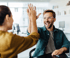Ein lächelnder Mann mit Brille und eine Frau geben sich im Büro ein High Five.