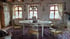 Ein rustikales Esszimmer mit einem ovalen weißen Tisch, vier Stühlen und einem gemusterten Teppich vor drei Fenstern.