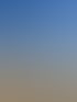 Frau in orangefarbener Jacke steht an einem Sandstrand und blickt auf das wellige Meer unter blauem Himmel.