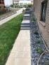 Gepflasterter Gartenweg mit dunklen Blockstufen neben einer Backsteinwand und einem Kiesbeet mit Pflanzen.