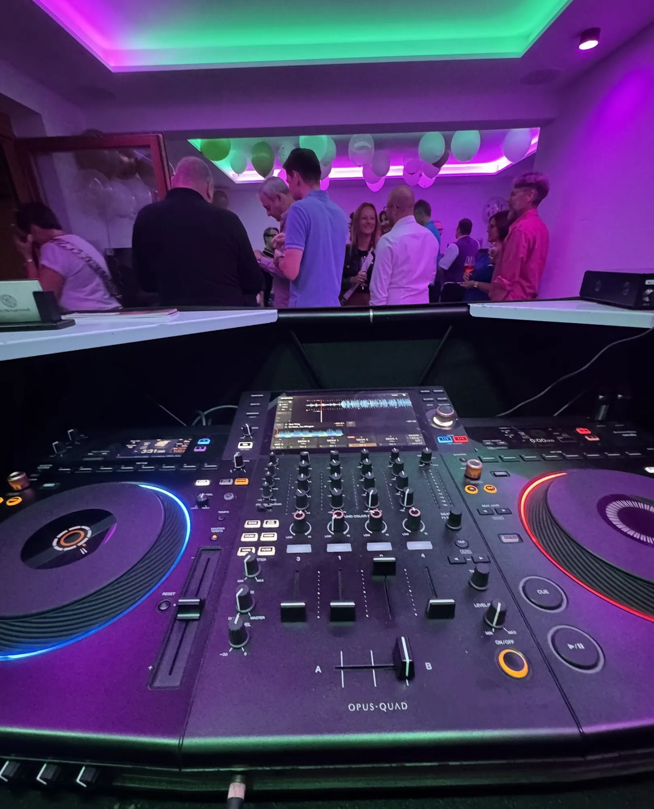 Feiernde Gäste vor dem DJ-Pult mit bunter Lichtshow