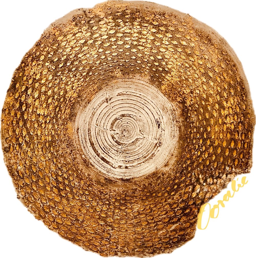 Runde, goldene, strukturierte Schale mit weißen Ringen in der Mitte und „Coralie“ Schriftzug.