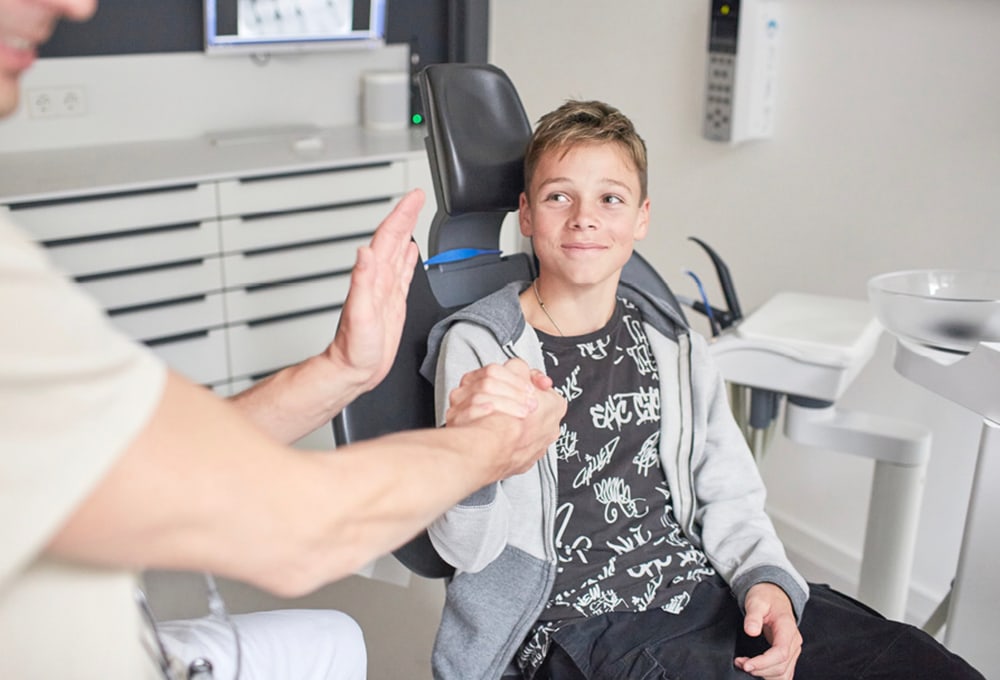 Kind gibt dem Zahnarzt auf dem Behandlungsstuhl ein High Five