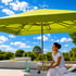 Grüner quadratischer Sonnenschirm über einer lächelnden Frau in Weiß, die auf einer Terrasse sitzt und ein Getränk hält.