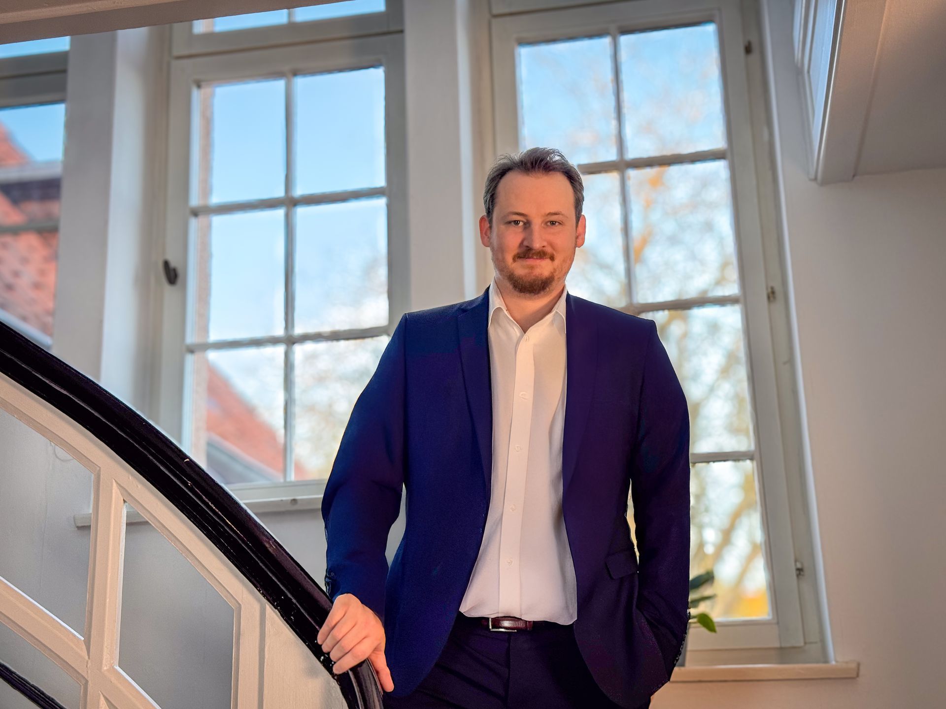 Immobilienmakler Niclas Marheineke begrüßt Kunden vor einem Haus