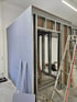 Trockenbauwand im Rohbau mit Metallständerwerk, blauen Gipsplatten und einer Leiter auf einer Baustelle.