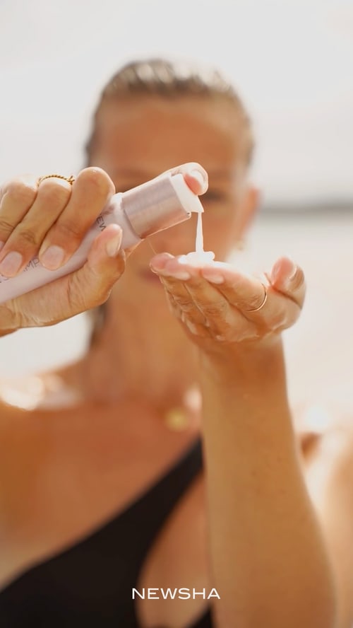 Eine Frau gibt eine weiße Lotion aus einem NEWSHA-Pumpspender direkt in ihre Handfläche.