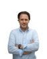 Mann mit dunklen Haaren und hellblauem Hemd lächelt, Arme verschränkt.