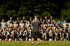 Ein Fußballtrainer steht vor einer großen Gruppe von jungen Fußballspielern auf einem grünen Feld.