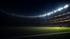 Fußballstadion bei Nacht mit hellem Flutlicht, das einen Teil des grünen Rasens und die Tribünen beleuchtet.