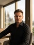 Mann im schwarzen Hemd sitzt am Tisch vor einem Fenster mit Blick auf den Kölner Dom.
