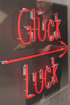 Rote Neonröhren formen die Wörter "Glück" und "Luck" mit einem Mann im Hintergrund.