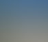 Weißes Haus mit rotem Ziegeldach, Veranda und zwei Bäumen davor, am Straßenrand unter blauem Himmel.