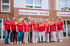 Gruppe von 16 Mitarbeitern in roten Hemden vor dem "Häusliche Pflege ROSE" Gebäude.
