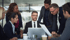 Six business professionals reviewing documents and a laptop in an office meeting.
