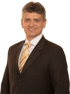 Juergen Graner in a dark pinstripe suit and a striped gold and brown tie smiles directly at the viewer.