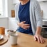 A person in a kitchen clutches their stomach while standing at a breakfast table with a bowl of oatmeal and berries.