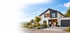 Modernes zweistöckiges weißes Einfamilienhaus mit Flachdach, großen Glasfronten, Garage und gepflegtem Garten bei Dämmerung.