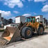 Gelber Radlader mit großer Schaufel auf einer Baustelle unter blauem Himmel mit weißen Wolken.
