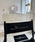 Schwarzer Stuhl mit weißem „BEAUTY ATELIER by Falia“-Logo vor einer weißen Theke mit gleichem Logo.
