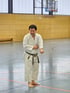 Keigo Shimizu Sensei im weißen Karate-Gi mit schwarzem Gürtel steht barfuß in einer Sporthalle und macht eine Faust.