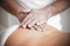 Hände eines Therapeuten führen eine manuelle Massage oder osteopathische Behandlung am unteren Rücken eines Patienten durch.
