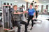 Eine Frau in Sportkleidung hilft einem Mann beim Training an einem Fitnessgerät.