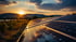 Solarpaneele spiegeln den Sonnenuntergang über einem Feld mit Bergen im Hintergrund wider.