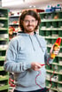 Ein lächelnder Mann mit Brille und Bart hält ein gelbes Multimeter mit roten und schwarzen Kabeln.