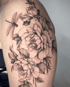 Detailliertes schwarzes Tattoo auf einer Schulter mit Pfingstrosen, Blättern und einer Libelle im Dotwork-Stil.