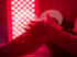 Person's hands and leg in front of a rectangular red light therapy panel.
