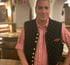 Ein Mann in traditioneller karierter Tracht und schwarzer Weste lächelt in einem Restaurant.
