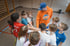 Ein erwachsener Mann mit "SCHOOL" auf dem Shirt und Kinder stehen im Kreis, die Hände in der Mitte übereinandergelegt.