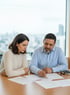 Ein Mann und eine Frau sitzen an einem Tisch und sehen sich Dokumente an. Der Mann zeigt mit dem Finger auf ein Blatt.