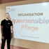 Mann lächelt neben einer Präsentation mit dem Titel "ORGANISATION queersensible Pflege".